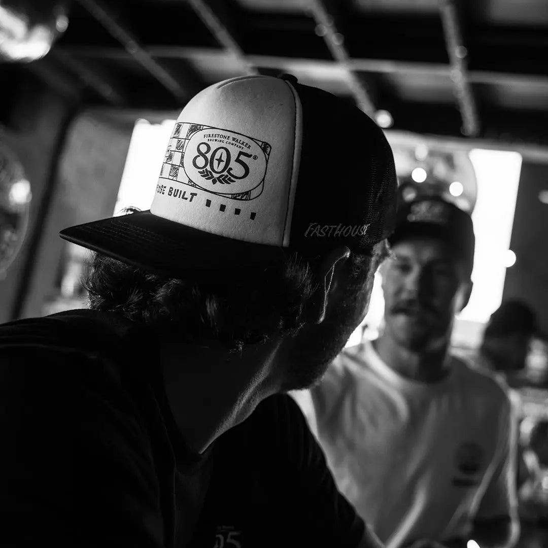 Person wearing 805 Purpose Black Hat, Garage setting with vintage racing memorabilia and industrial lighting in background -