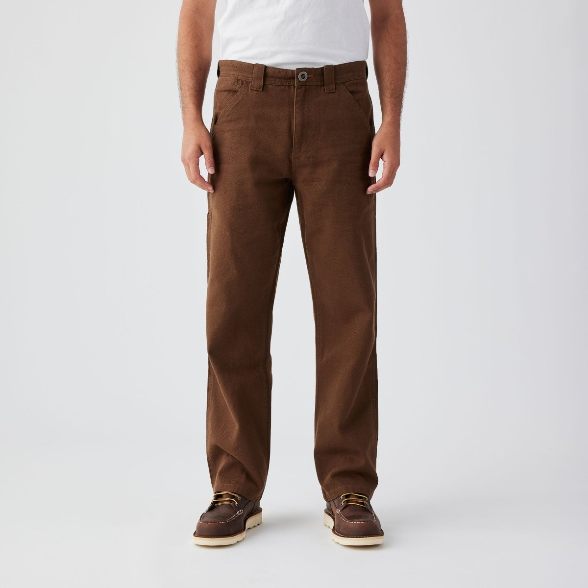 Person wearing Bison Canvas Pants Brown Pants, Man standing against neutral backdrop wearing brown canvas pants with white