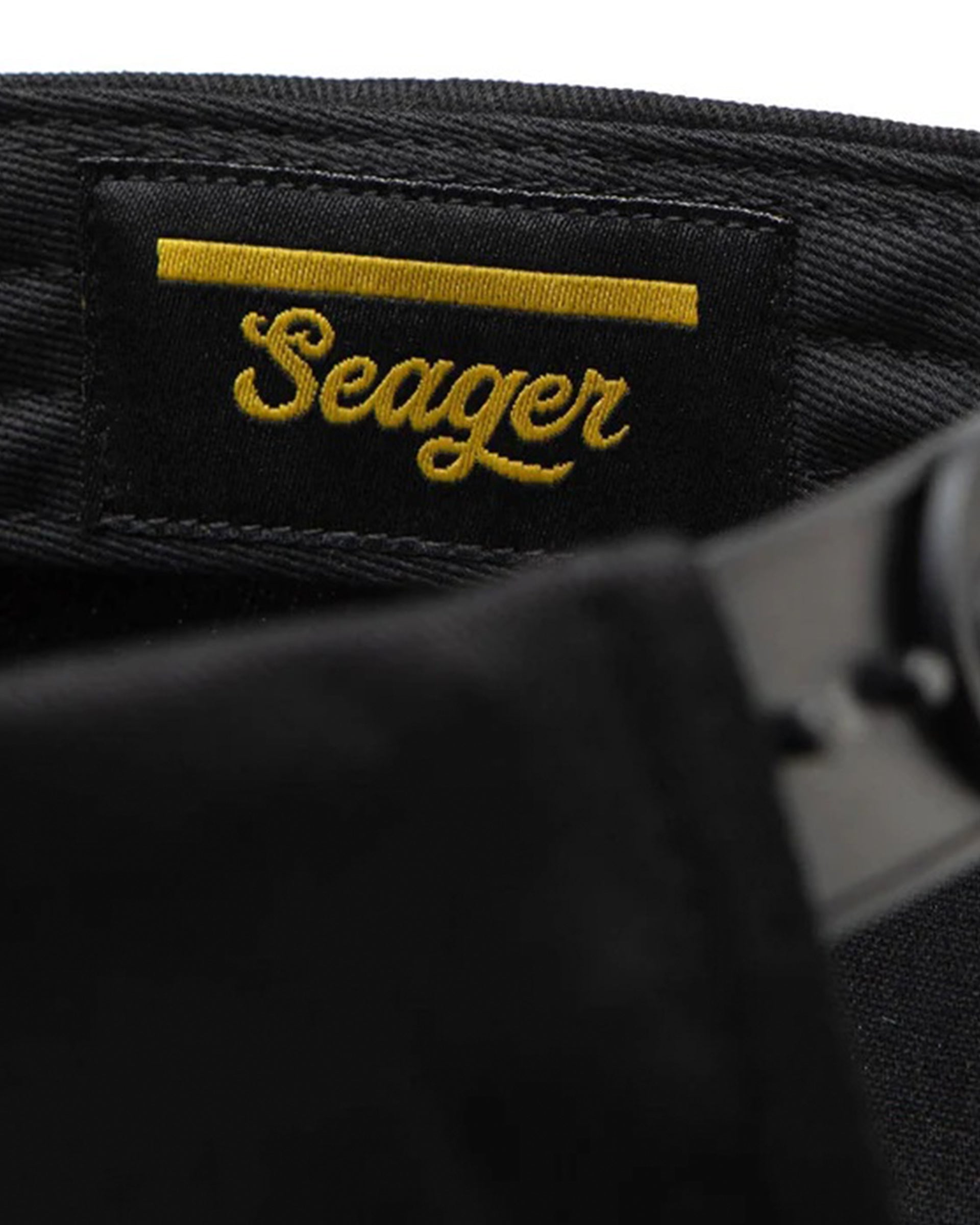 Care label on Bradley Snapback Black Hat showing Black woven label with gold embroidered script text and horizontal stripe
