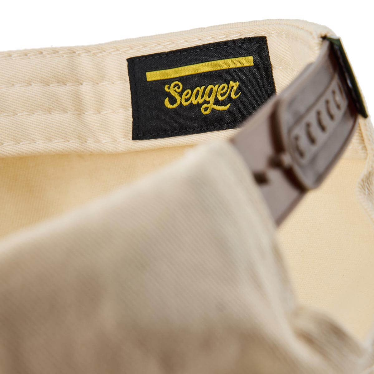 Care label on Branded Snapback Hat Apparel Cream/Camo Apparel showing Black label with yellow stripe and cursive script text