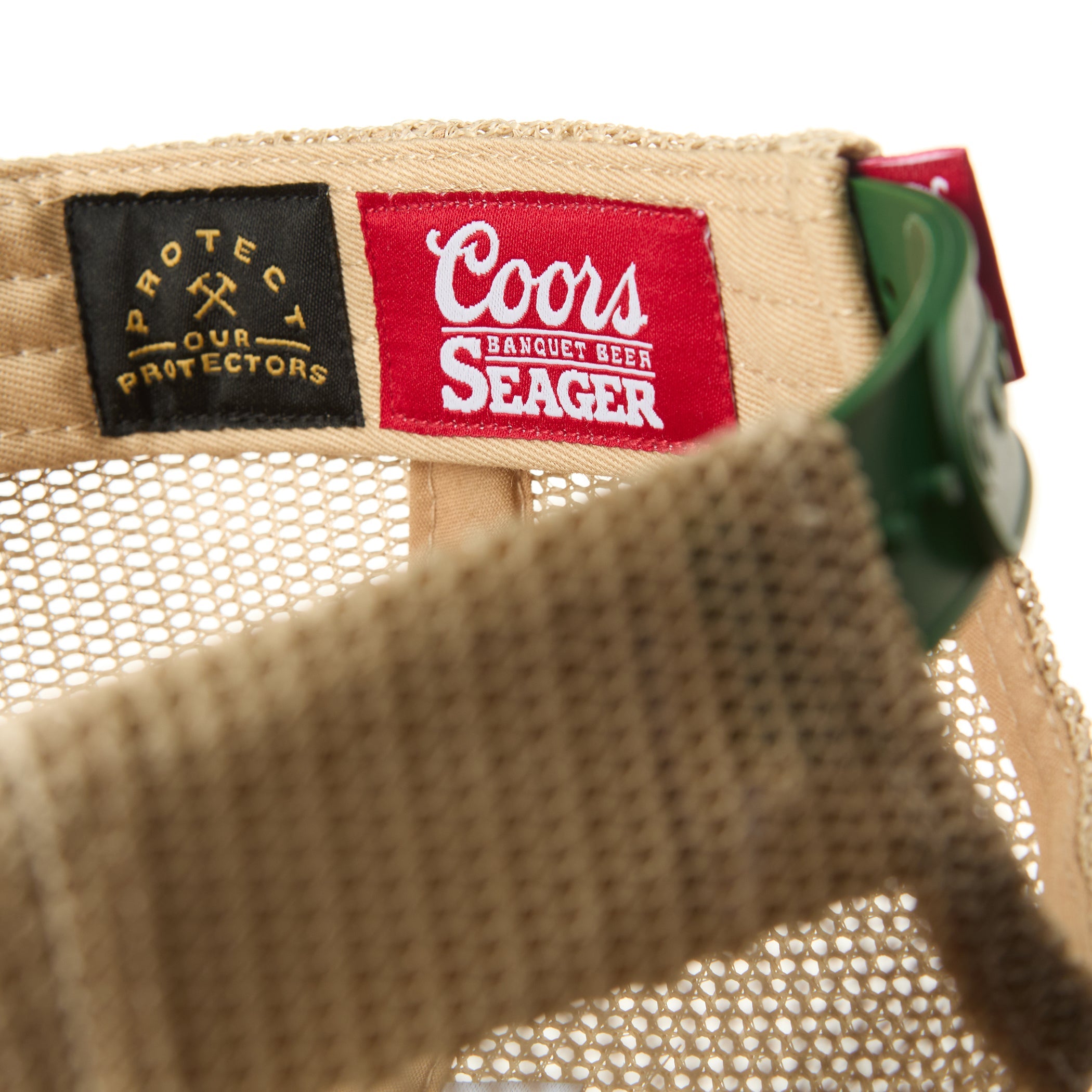Care label on Coors Banquet Helo Trucker Green Hat showing Black label with gold crossed pickaxes and text, red label with