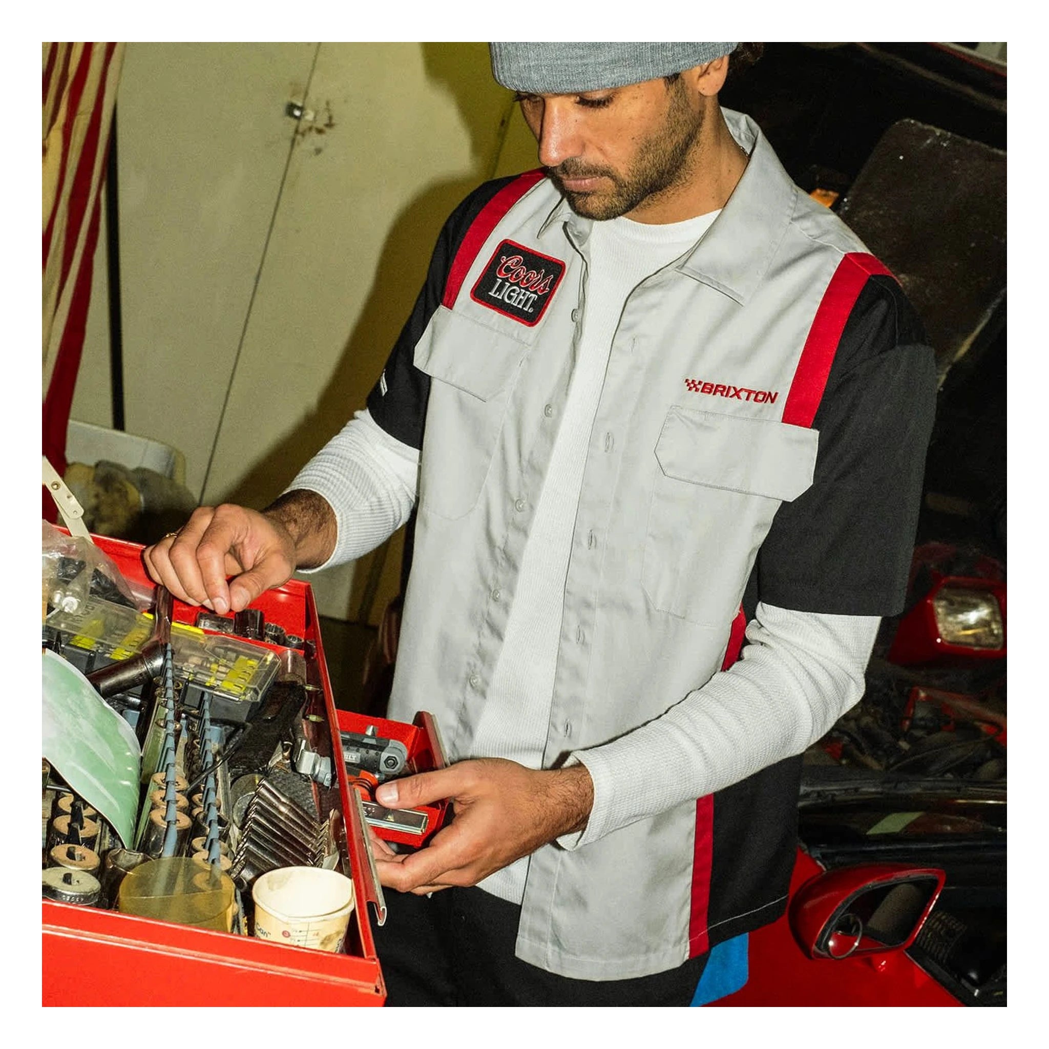 Person wearing Coors Light Shake Down S/S Woven Silver/black S/S Woven, Man working on engine in garage workshop setting -