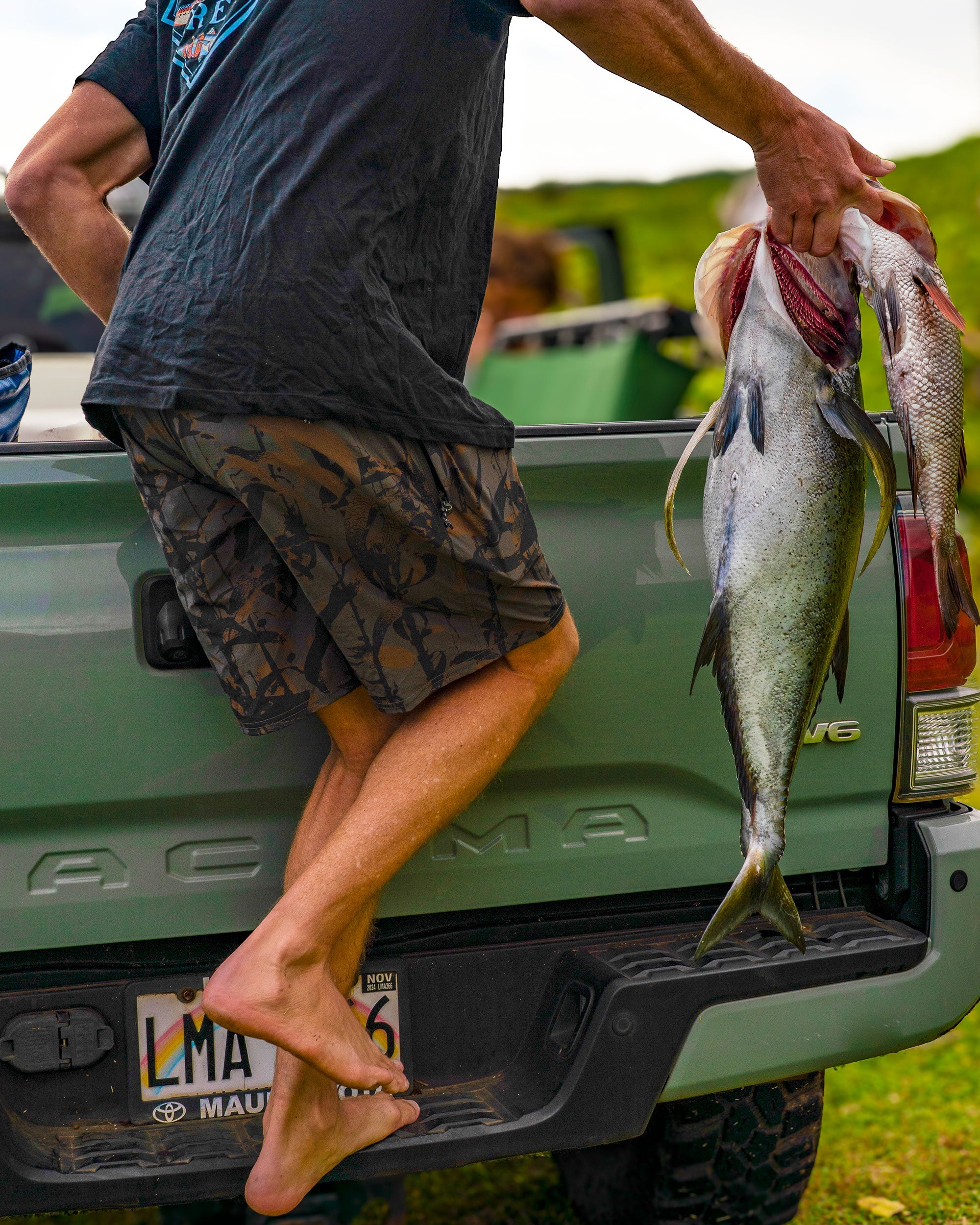 Person wearing Crew Boatshort 18" Boardshorts Camo Boardshorts, Man in fishing truck bed holding freshwater catch, rural
