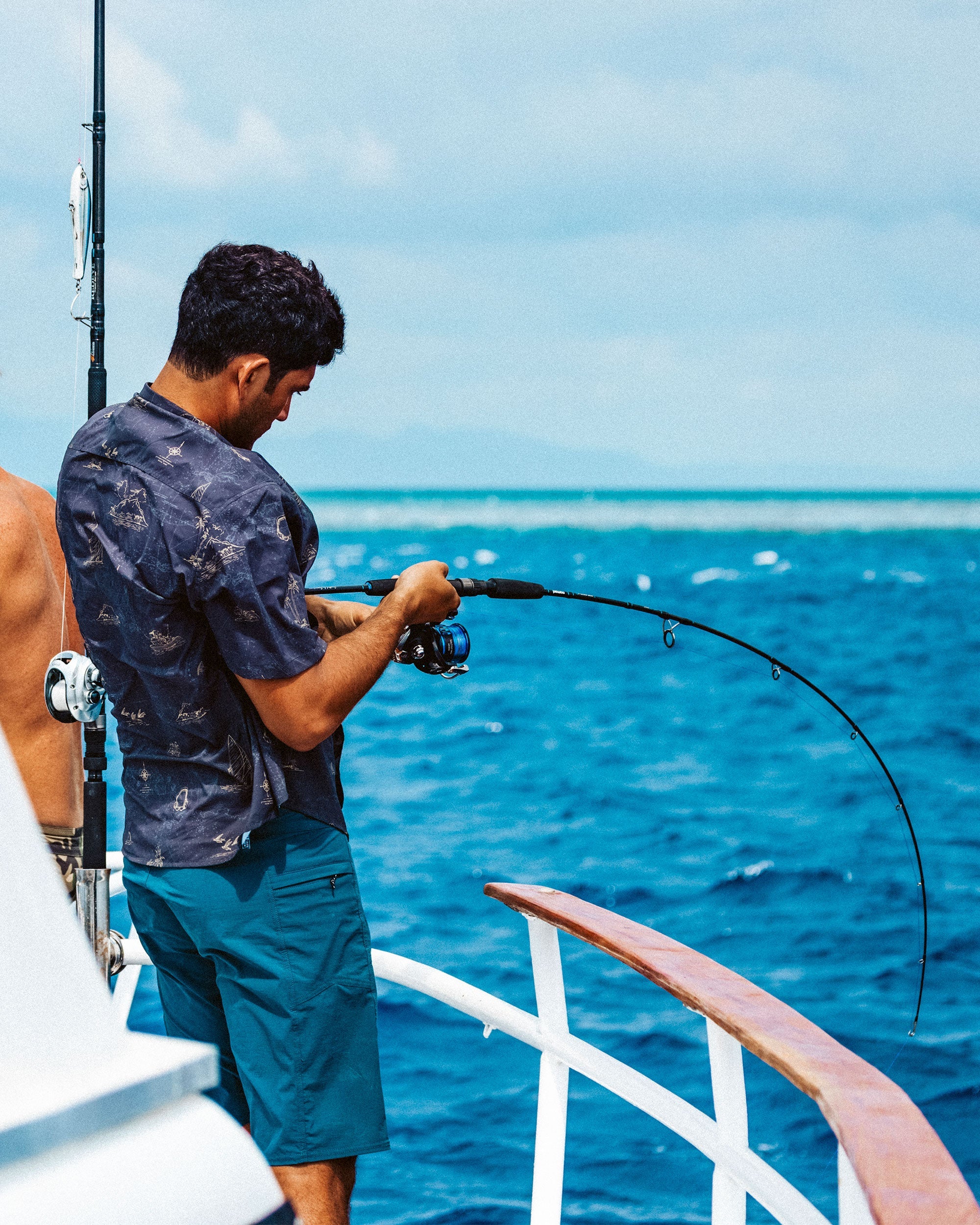 Person wearing Flagship Boatshort 19" Boardshorts Navy Boardshorts, Man fishing on open ocean boat with clear blue water and