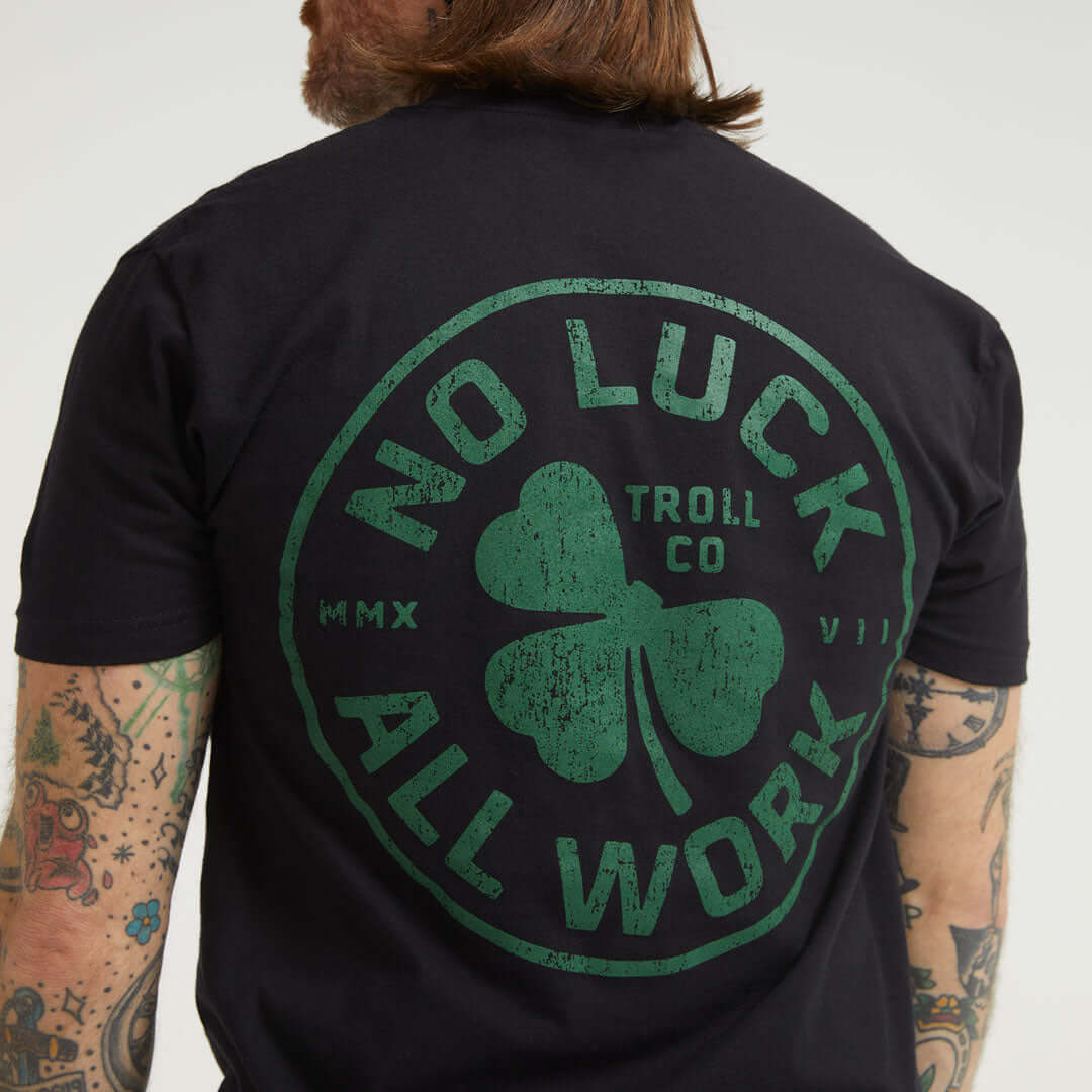 Person wearing Hardluck Black Tee, Worn while standing indoors against neutral backdrop, arms visible with tattoos -