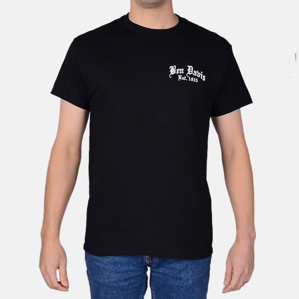Person wearing Paisley Black Tee, Man wearing black tee with white chest print, standing in neutral studio setting -