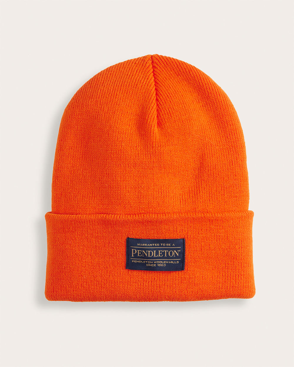 Back of Red Beanie, Bright orange knit beanie with navy woven label on cuff reading warranty text and manufacturer details -