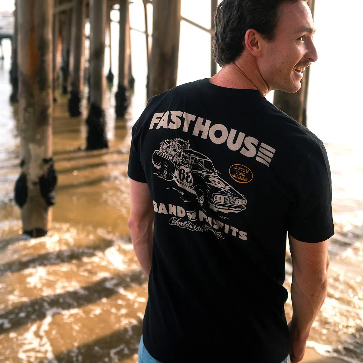Person wearing Pursuit Natural Tee, Man wearing black tee under a wooden pier with water and pilings visible - Slowride