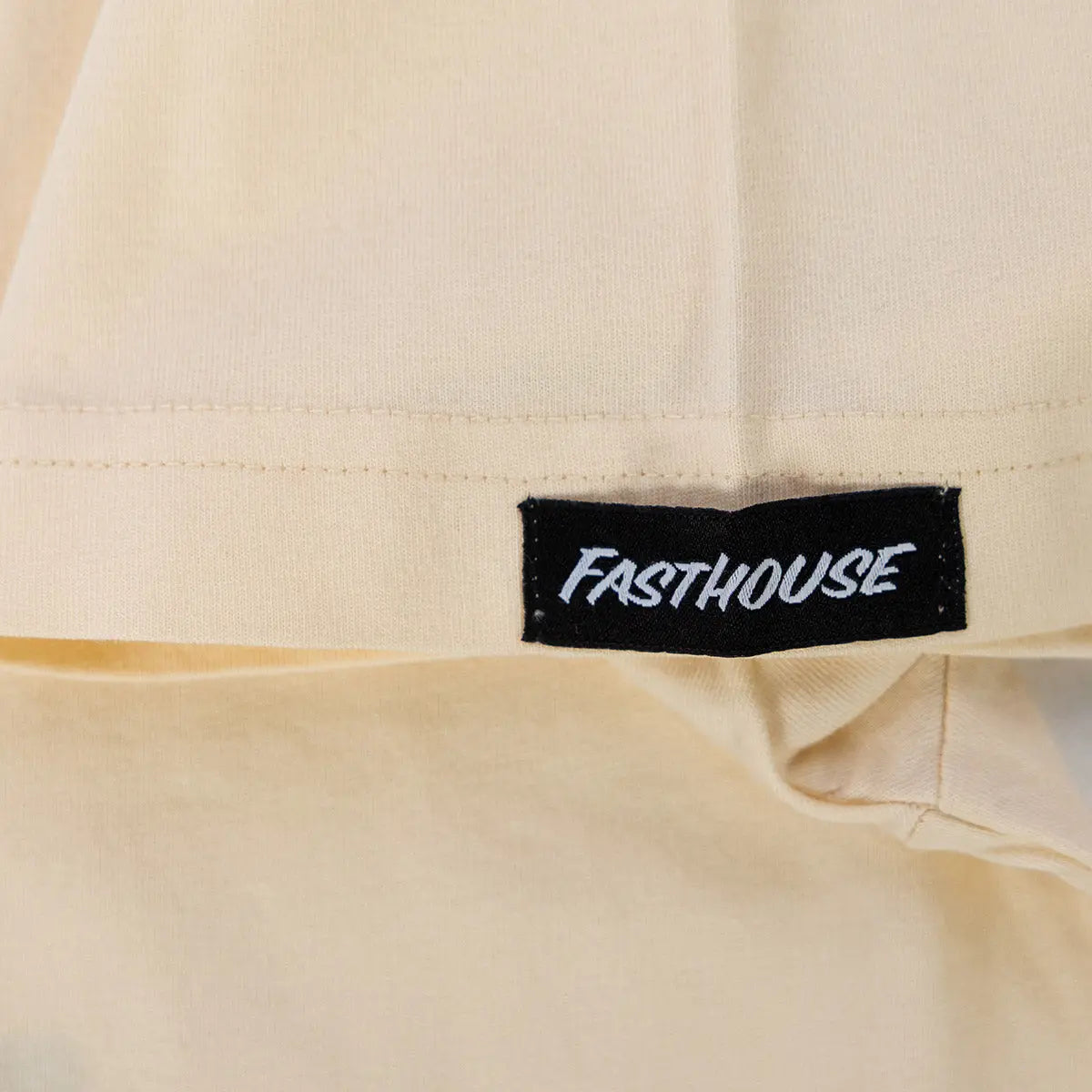 Care label on Pursuit Natural Tee showing Black woven label with white italic text on cream garment - Slowride Supply