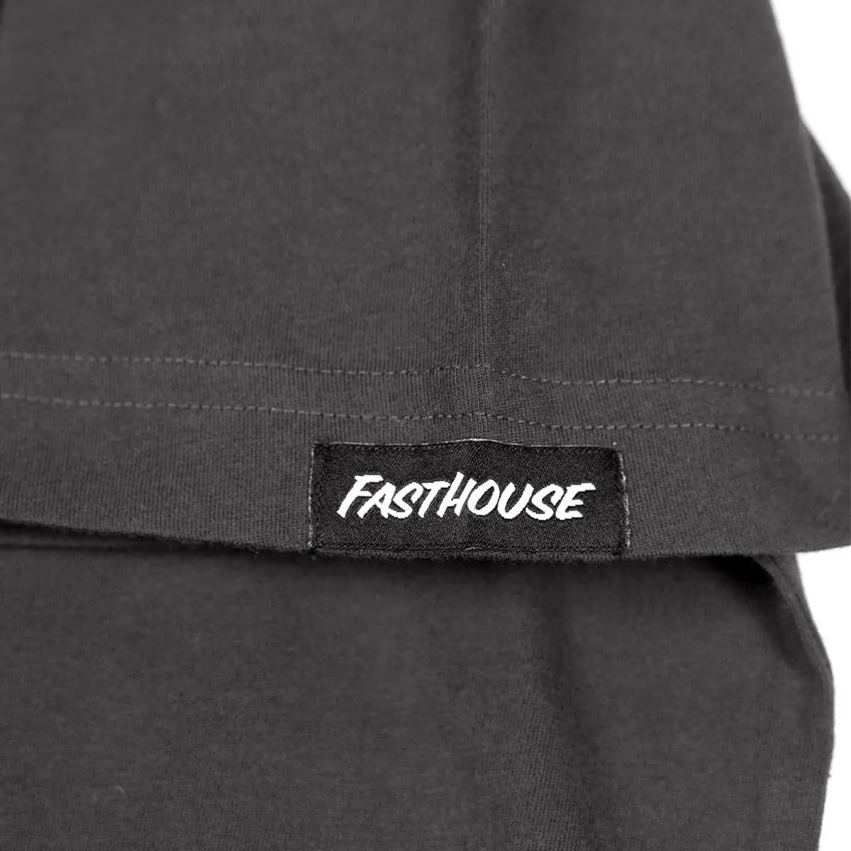 Close-up of Record Natural Tee showing Black woven label with white italic text on charcoal cotton fabric with visible