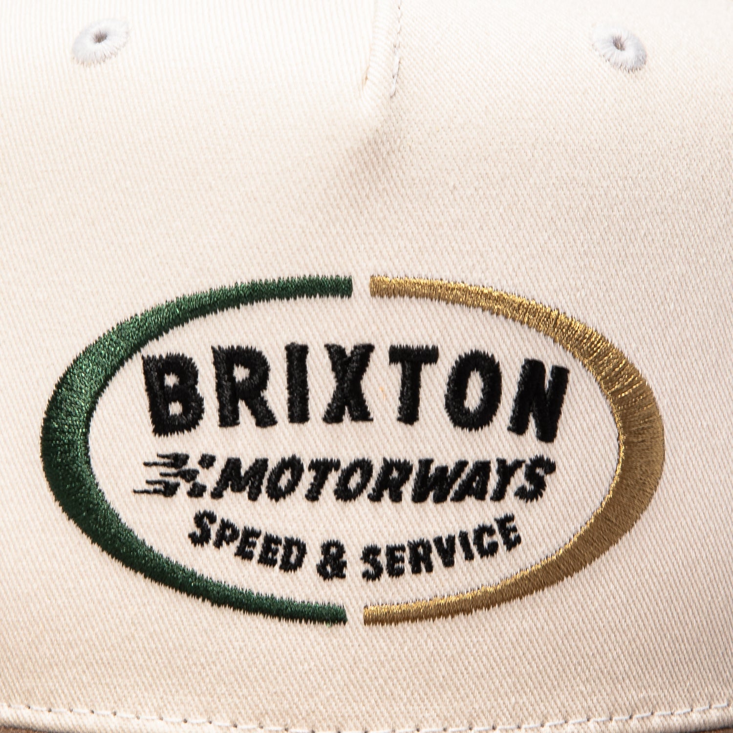 Close-up of Rhett MP Snapback Off White/pinecone Brown Hat showing Embroidered oval logo with green and gold border, black