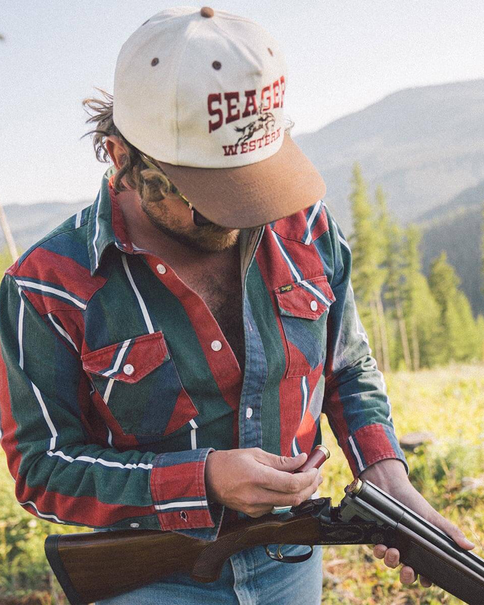 Person wearing Rodeo Snapback Cream/brown Hat, Mountain landscape with evergreen trees and rolling hills in background -