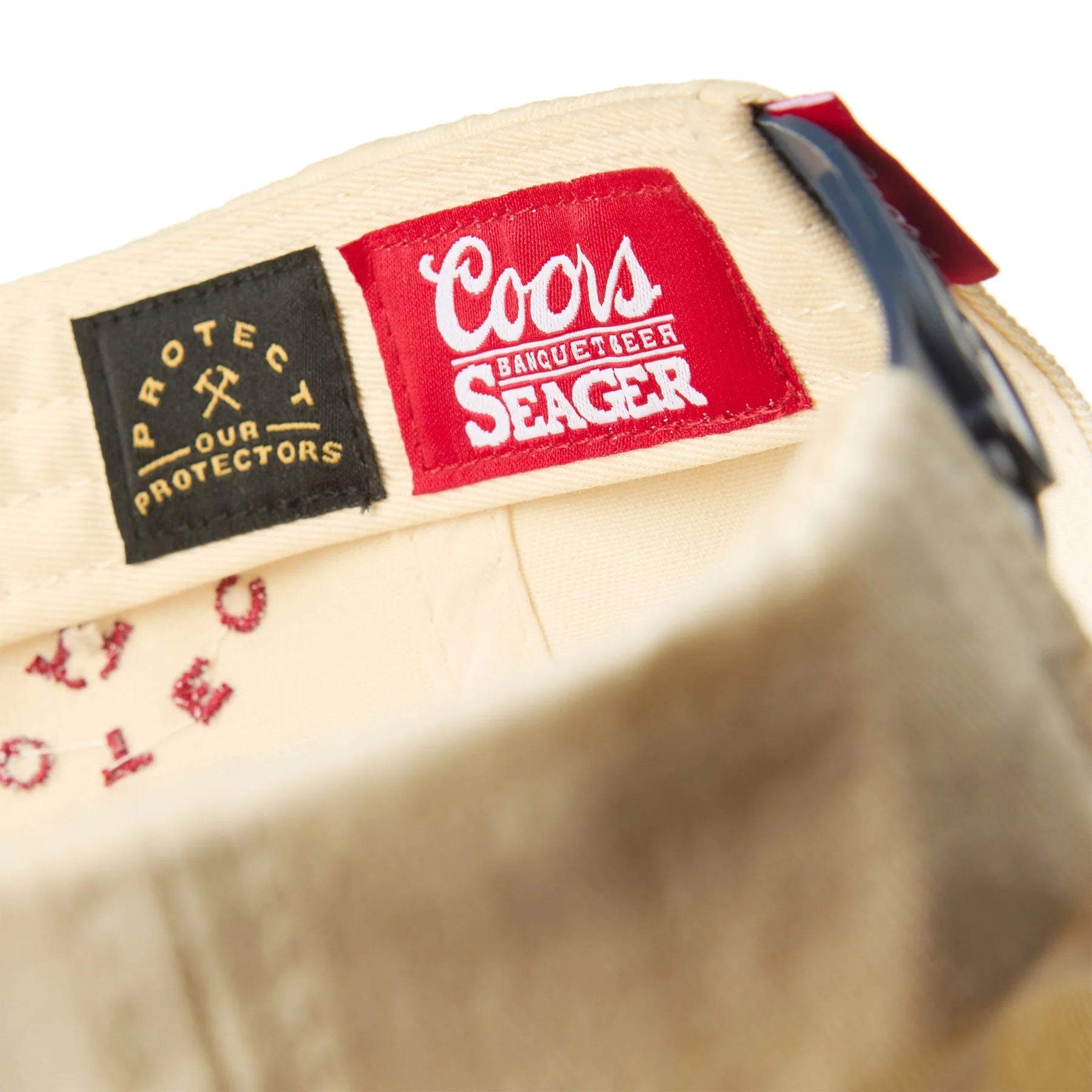 Care label on X Coors Banquet P.o.p. Snapback Cream/navy-cream/navy Hat showing Woven red label with white script logo and