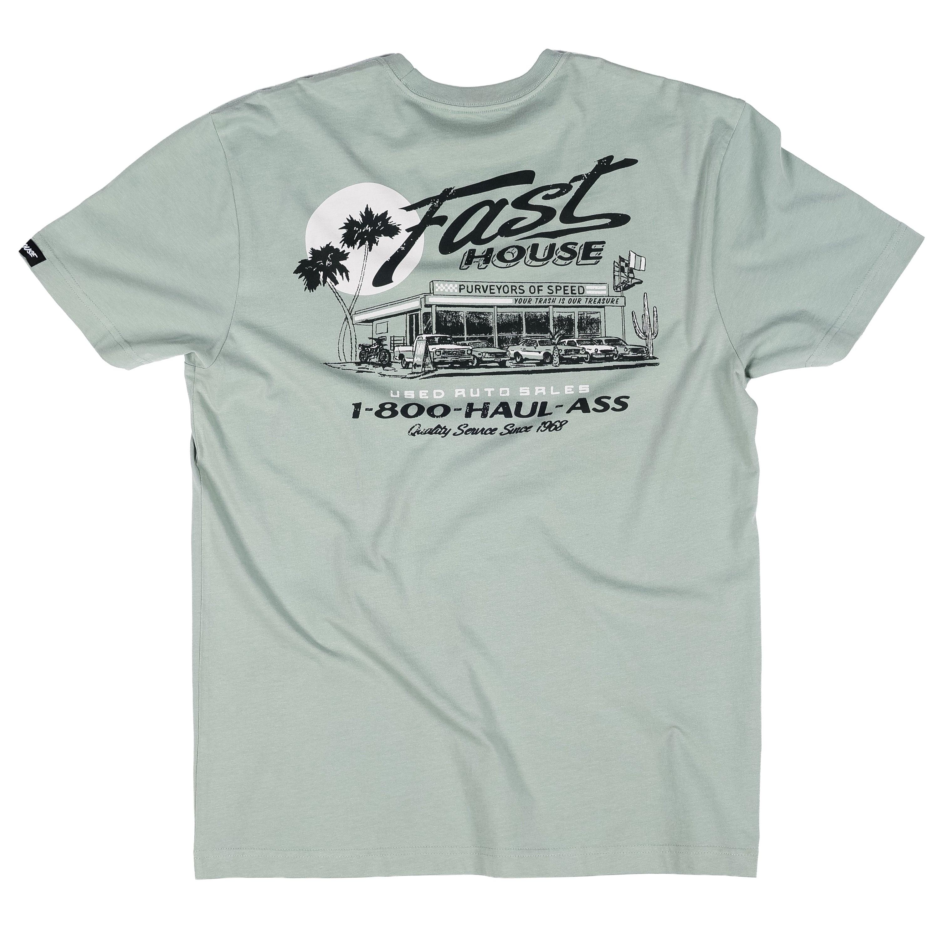 Close-up of Sunset Black Tee showing Sage green with black line-art graphic depicting vintage auto dealership storefront,