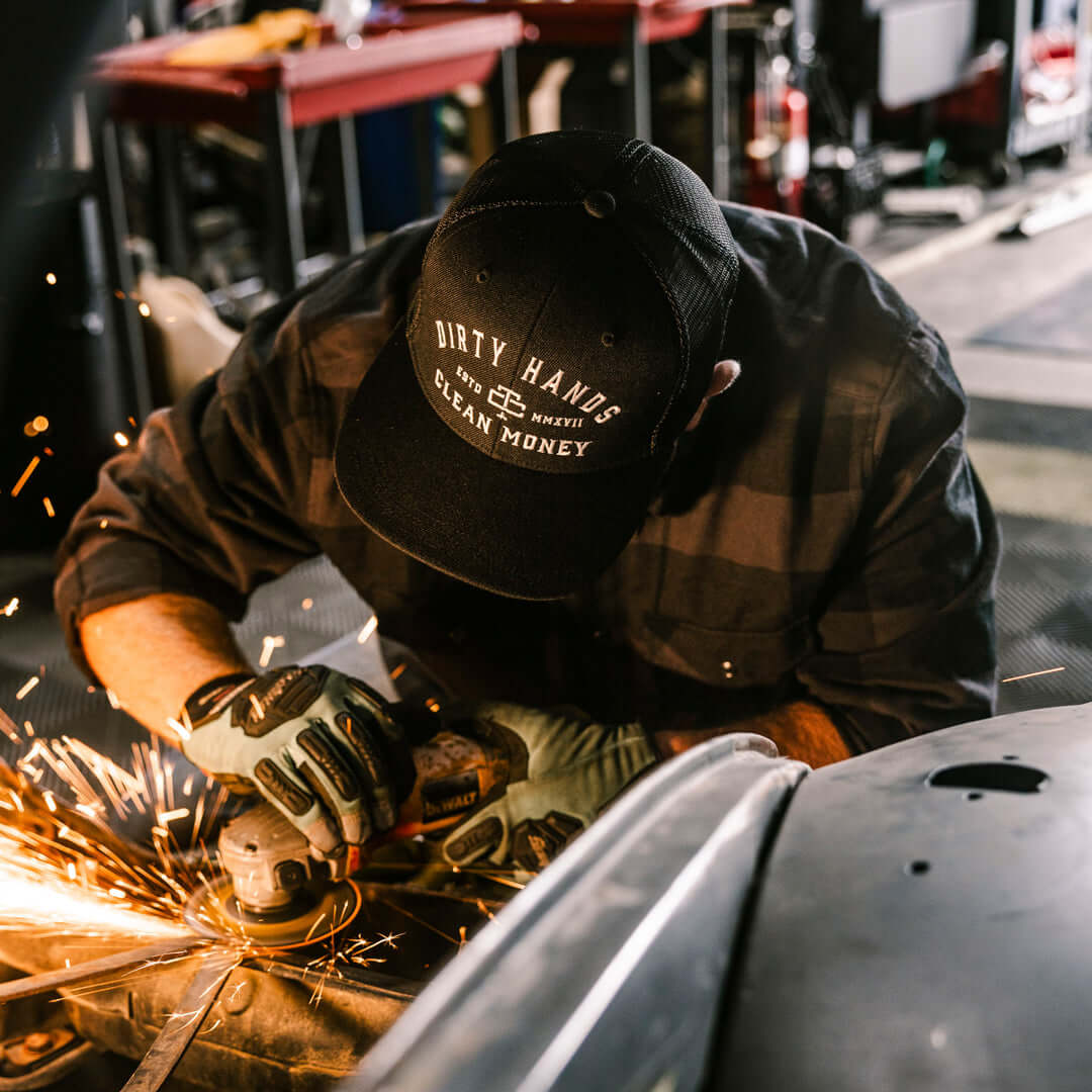 Person wearing DHCM Classic Trucker White/coyote Brown Hat, Mechanic welding in an industrial garage workshop setting -
