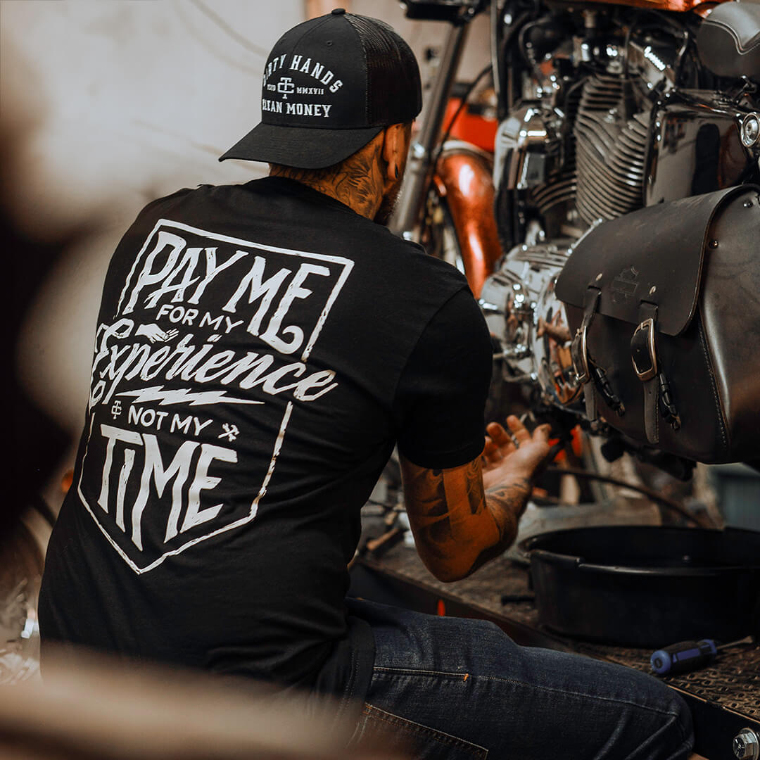 Person wearing DHCM Classic Trucker White/coyote Brown Hat, Garage workshop with custom motorcycle and engine visible in