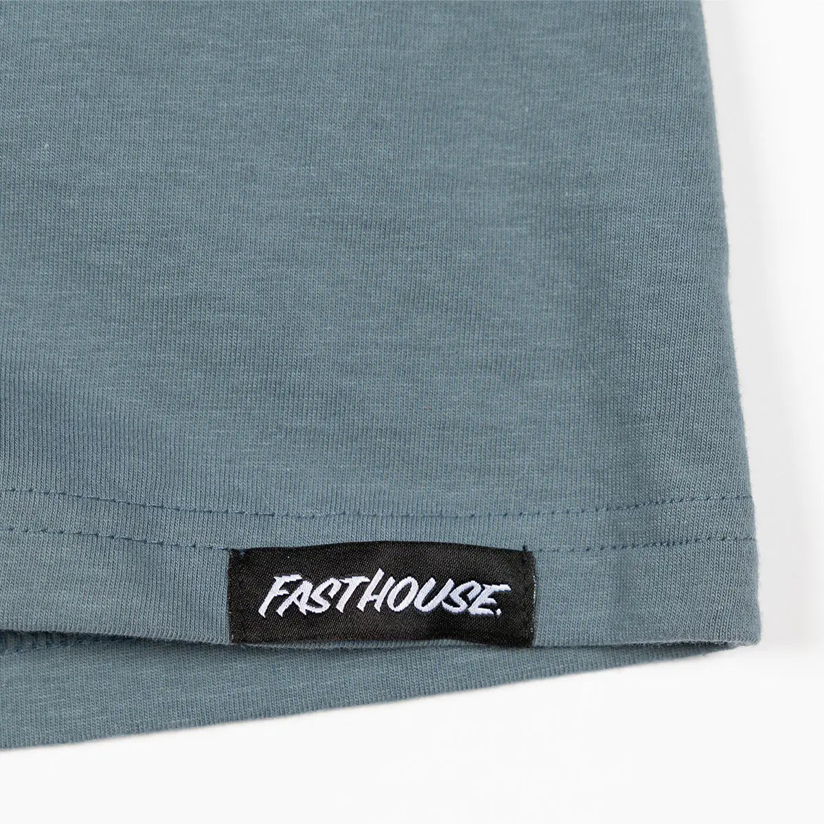 Close-up of Trust Tank Apparel Indigo Apparel showing Black woven label with white script text on ribbed hem edge - Slowride