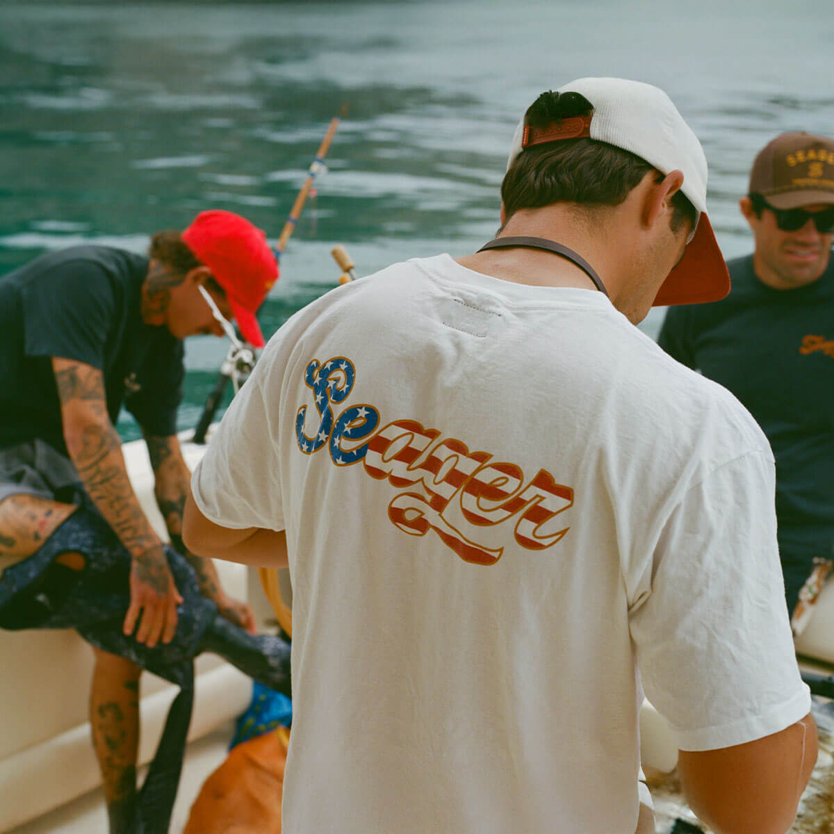 Person wearing USA Russ Vintage Black Tee, Fishing boat on open water with multiple people in casual attire - Slowride Supply