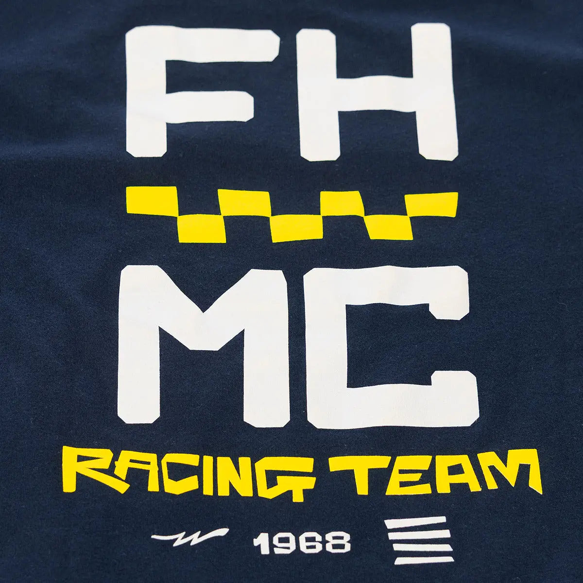 Close-up of Youth Team Tee Navy Kids Navy Kids Tee showing White and yellow printed graphic with "FH MC" letters, checkered