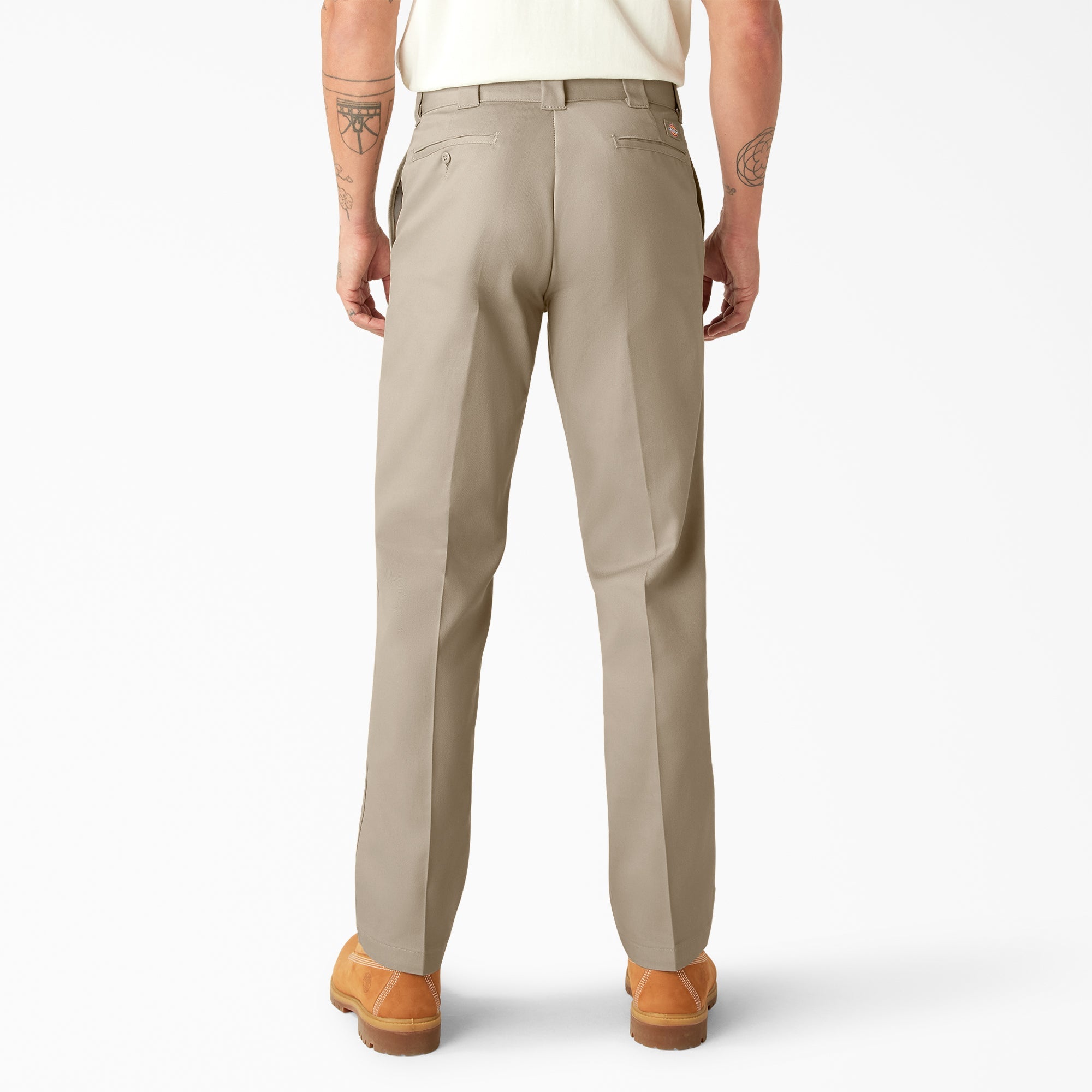Person wearing 874f - Flex Work Pant Pants Dark Navy Pants, Man wearing cream tee and tan work pants, standing against white