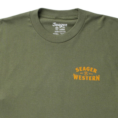 Close-up of Americas Choice Surplus Green Tee showing Surplus green cotton tee with gold chest print reading "Seager