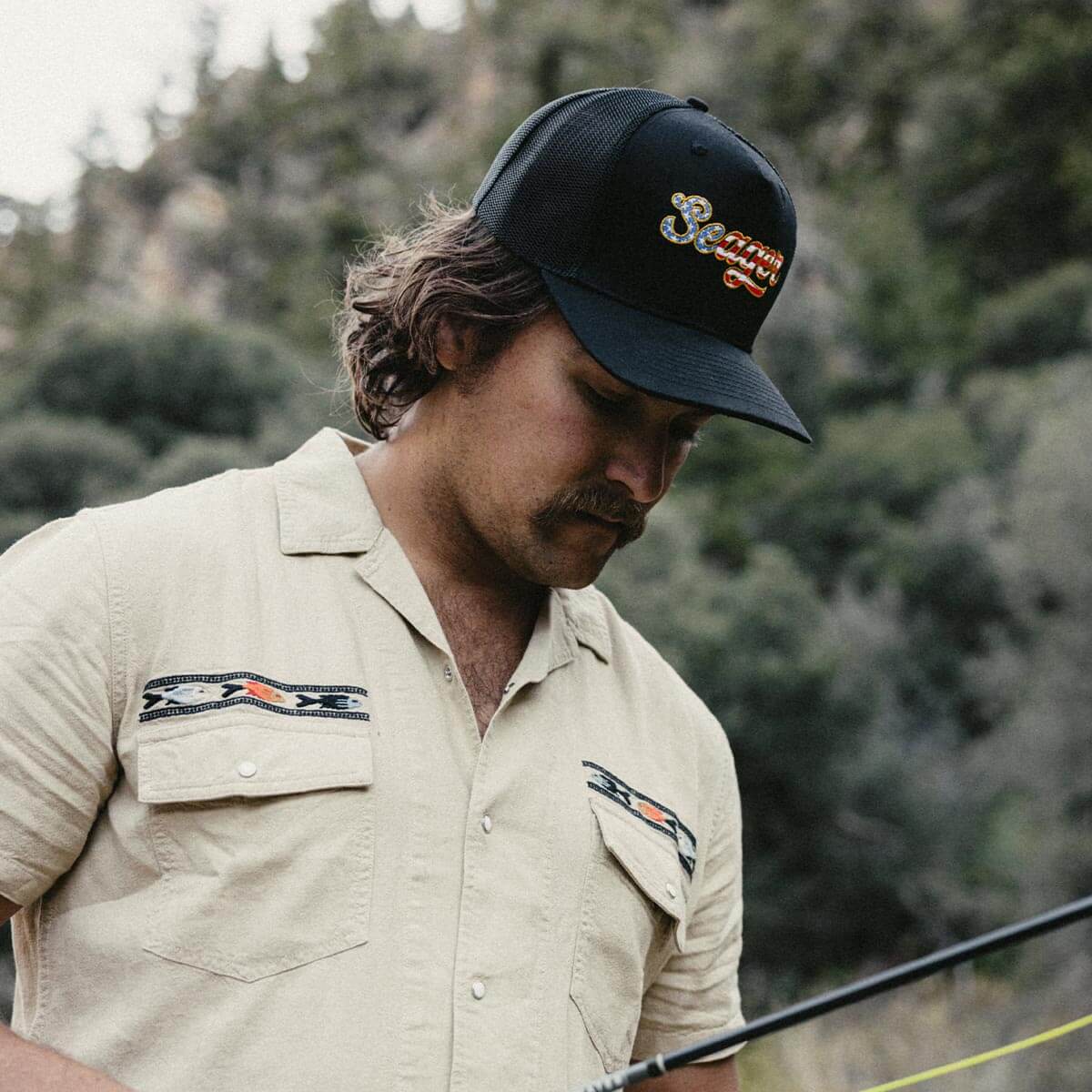 Person wearing Big USA Snapback Black Hat, Forested mountain setting with evergreen trees in soft daylight - Slowride Supply