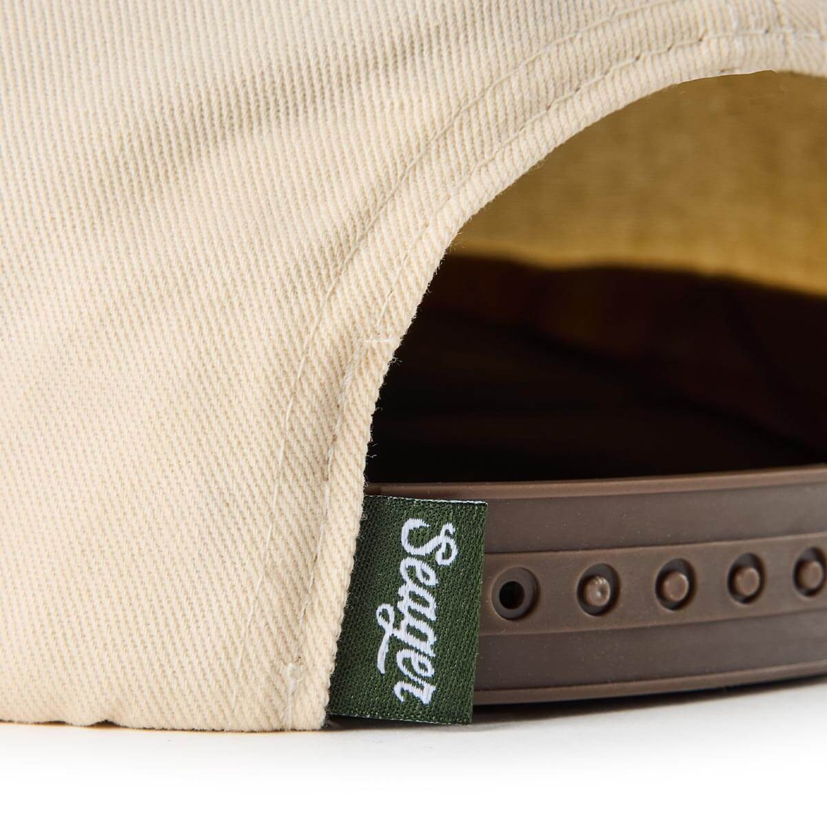 Close-up of Branded Snapback Hat Apparel Cream/Camo Apparel showing Green woven label with white script text on snapback hat