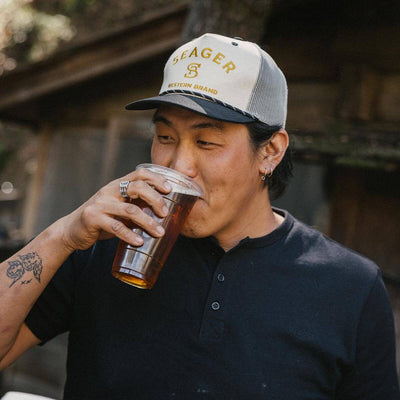 Person wearing Branded Snapback Hat Apparel Cream/Camo Apparel, Man wearing black henley shirt and cream trucker cap in