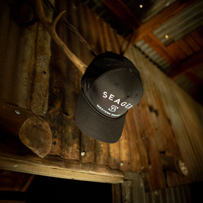 Close-up of Branded Trucker Black/Black Hat showing Black cotton twill cap with white embroidered front graphic and curved