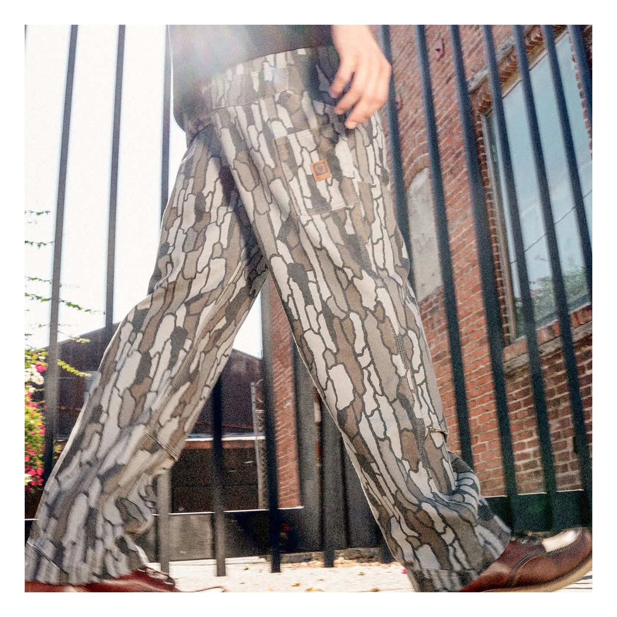 Person wearing Builders Carpenter Pant Pants Washed Black Pants, Brick industrial courtyard with metal fencing and climbing