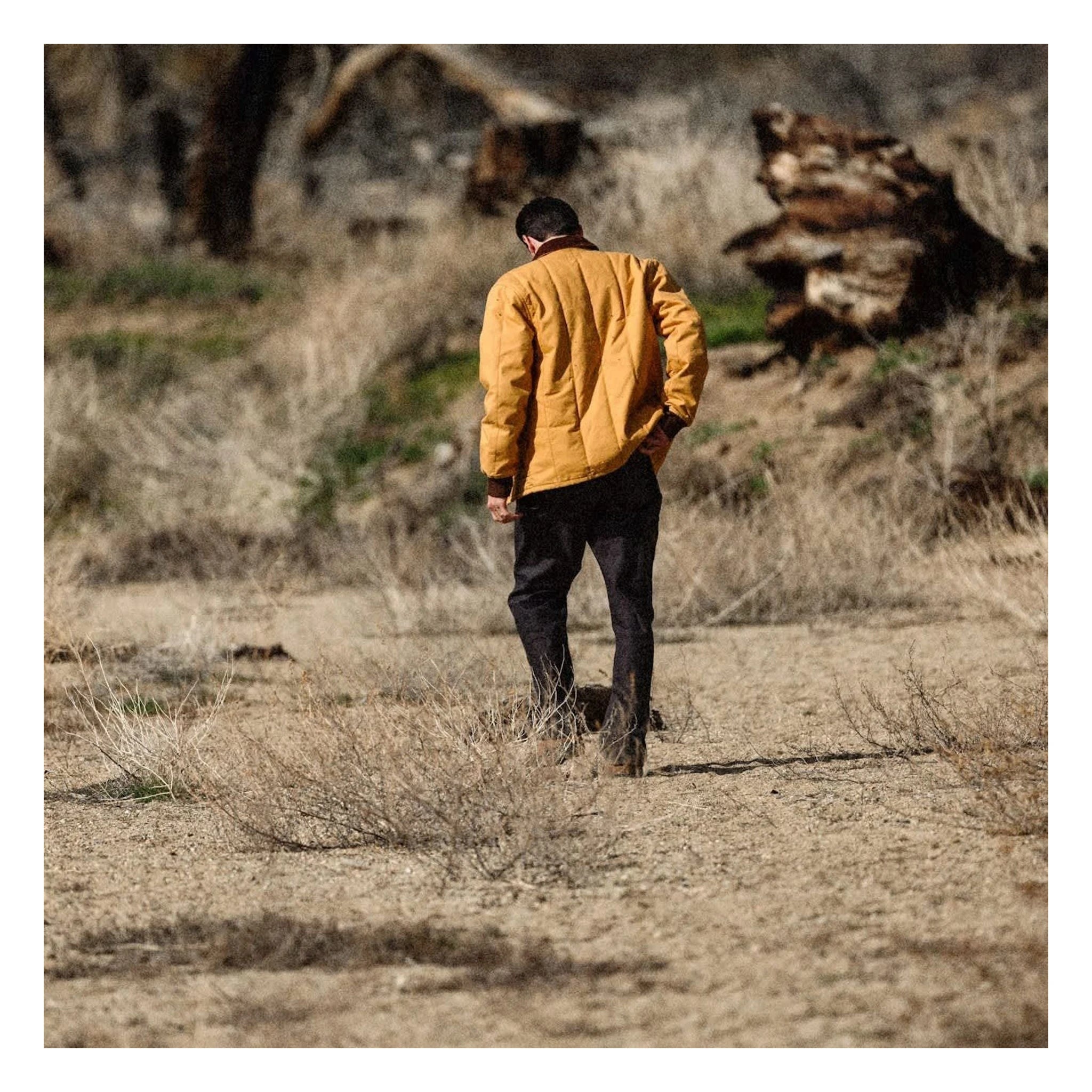 Person wearing Builders Ranch Jacket Spruce Yellow Jacket, Runner jogging through desert terrain with rocky outcrops and