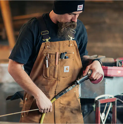 Person wearing Duck Bib Overalls Black Overalls, Man in work apron and navy shirt in industrial garage workshop setting -