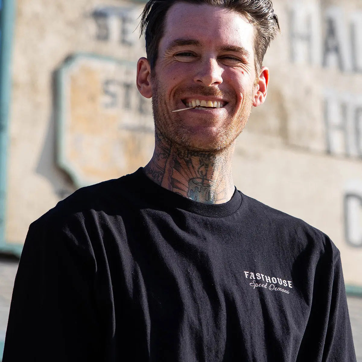 Person wearing Fallen Black Tee, Urban street setting with weathered concrete building backdrop - Slowride Supply