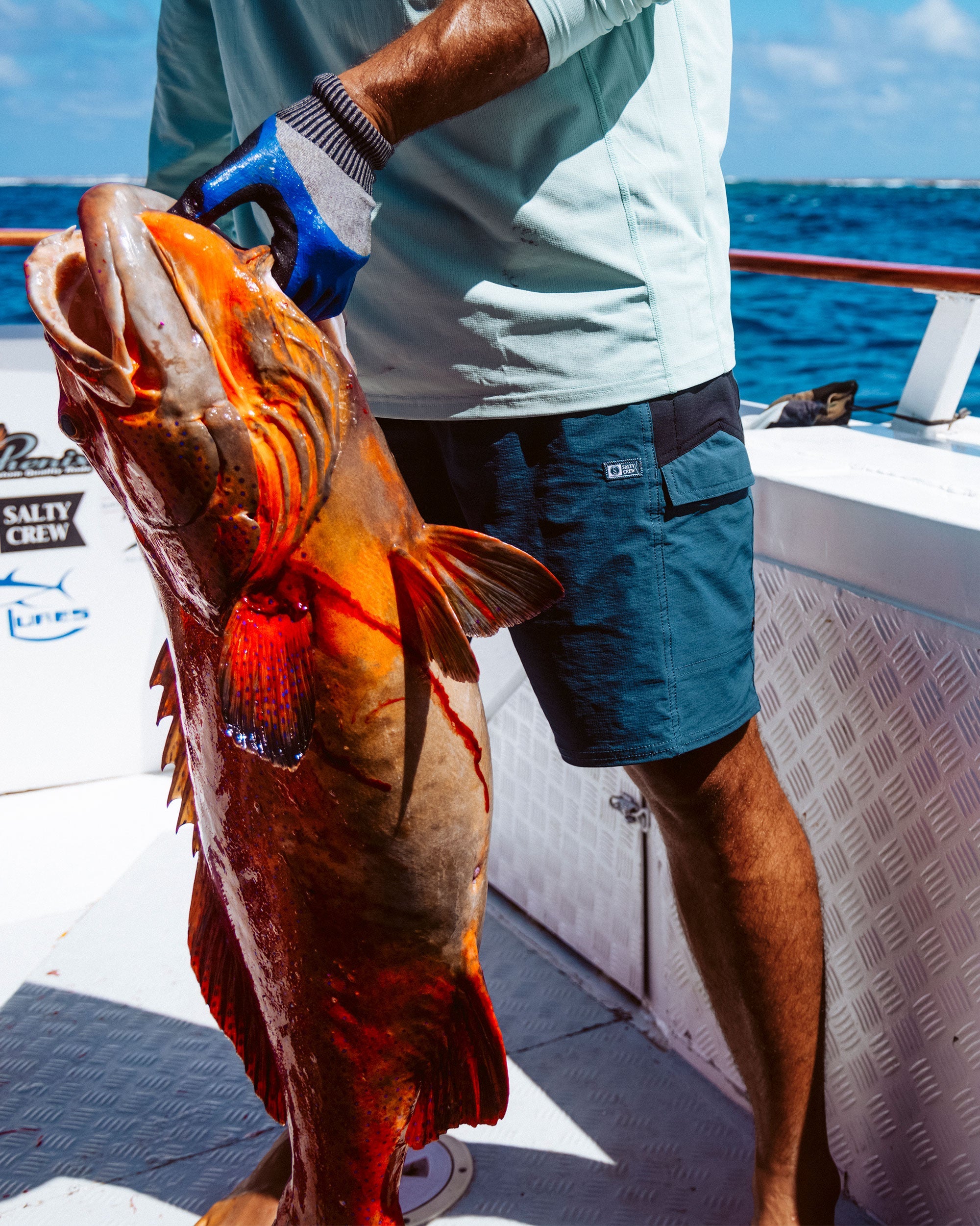 Person wearing Flagship Boatshort 19" Boardshorts Navy Boardshorts, Open ocean fishing boat with calm blue water and clear