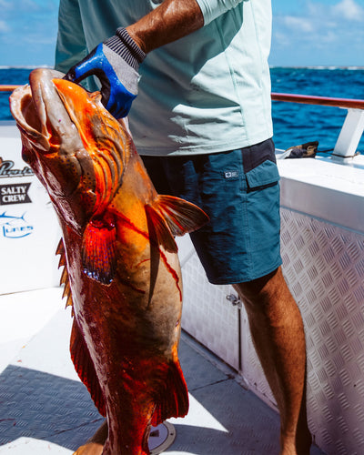 Person wearing Flagship Boatshort 19" Boardshorts Navy Boardshorts, Open ocean fishing boat with calm blue water and clear