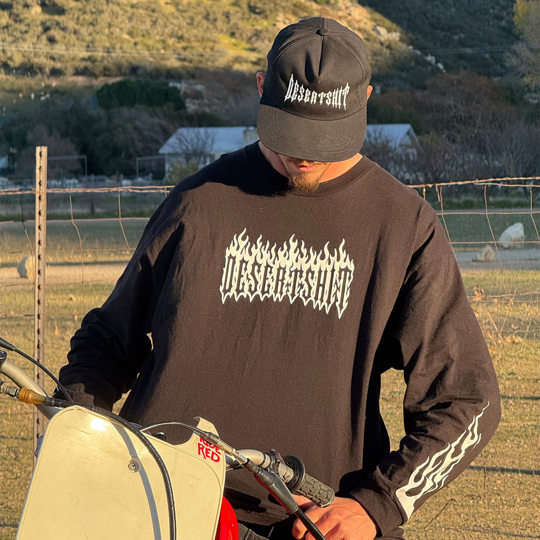 Person wearing Flames Black/white L/S Tee, Rural ranch setting with wooden fence, dry grass, and hillside in background -