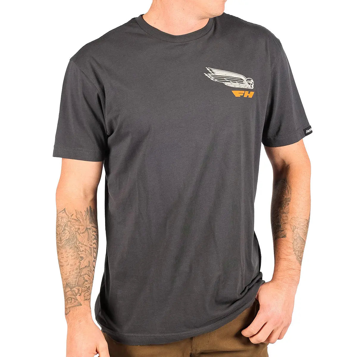 Person wearing Flyer White Tee, Man wearing charcoal tee with small chest graphic standing against white background -