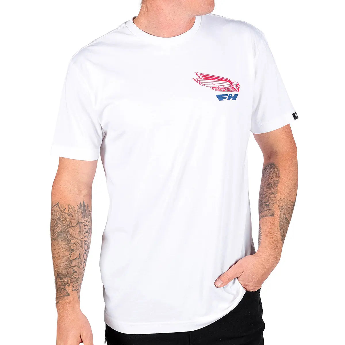 Person wearing Flyer White Tee, Man wearing white tee with red and blue winged graphic, posed indoors against neutral