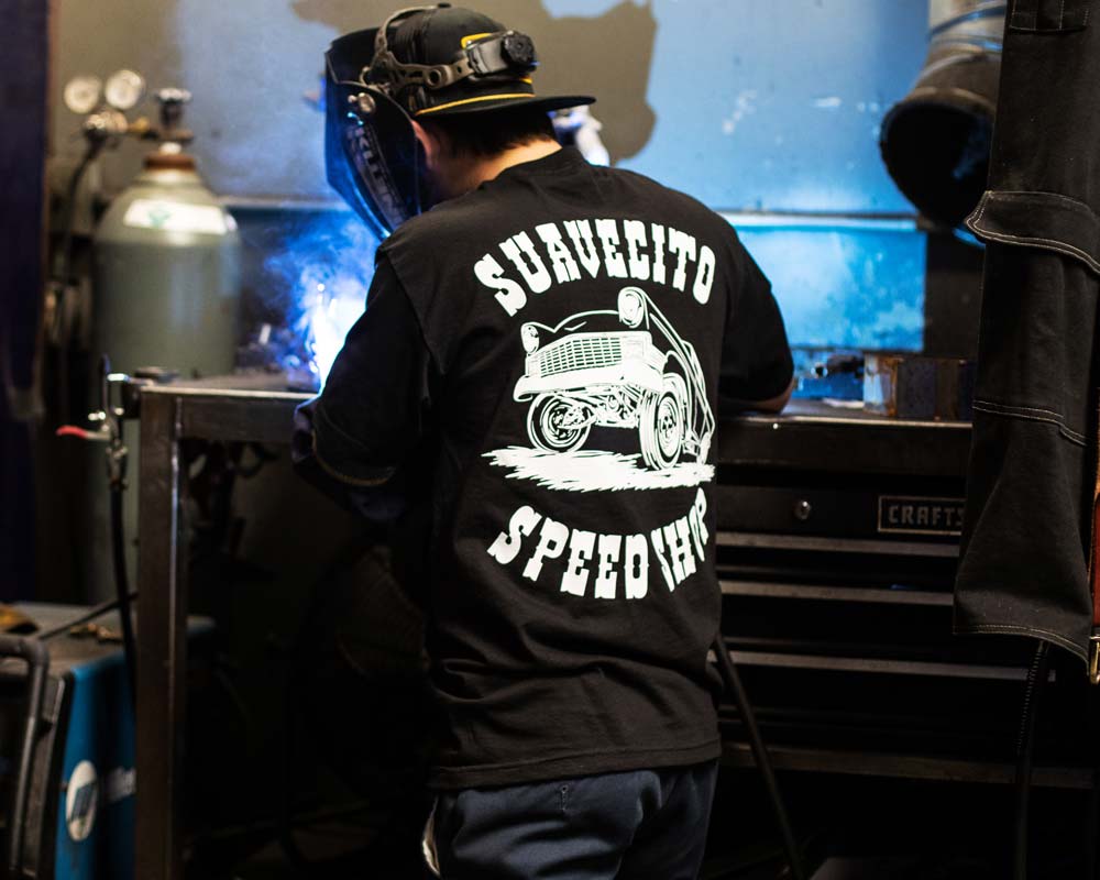 Person wearing Gasser Black Tee, Person wearing black tee in industrial garage workshop with welding equipment and toolbox -