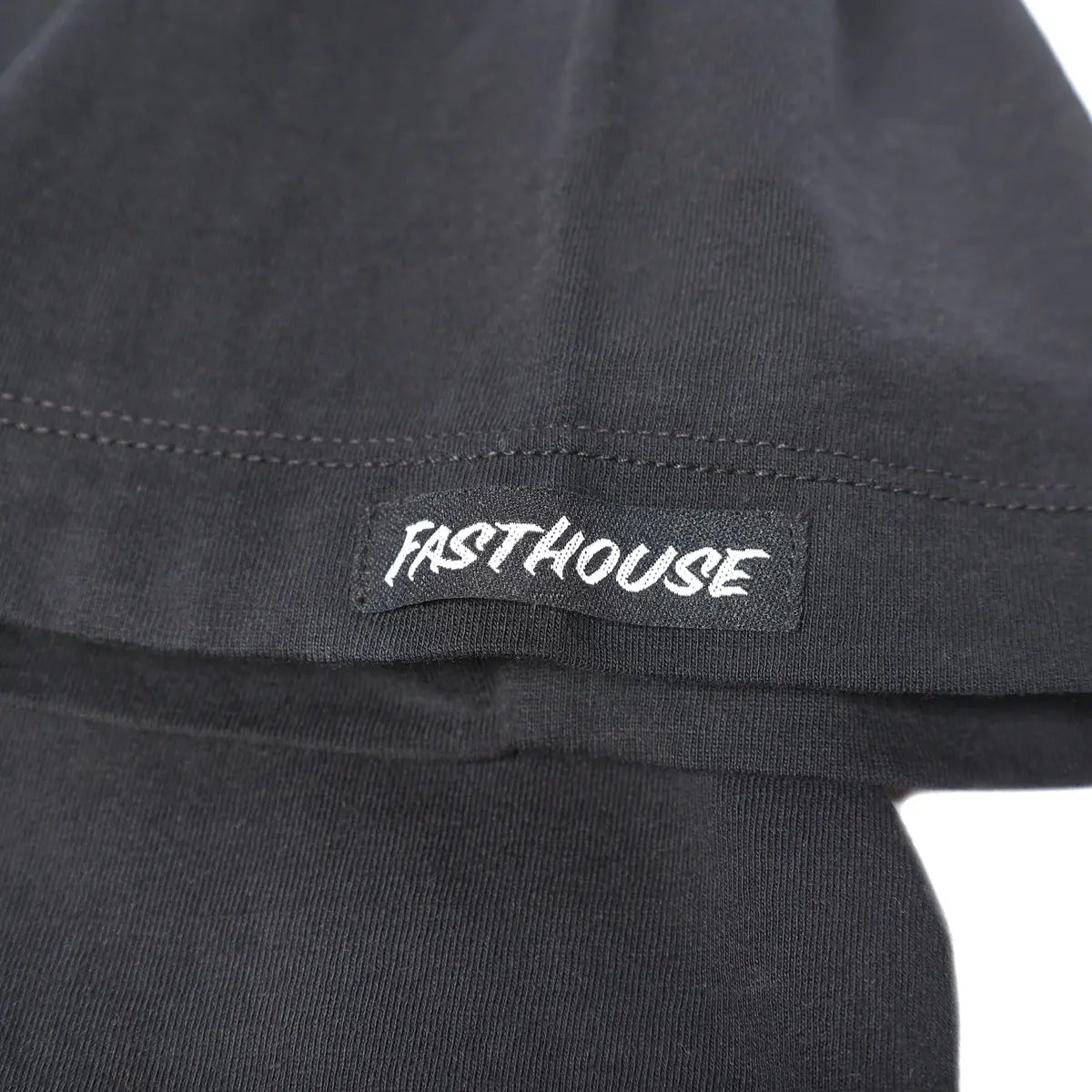 Close-up of Gilmore Black Tee showing White embroidered text on black sleeve with visible stitch detail and seaming -