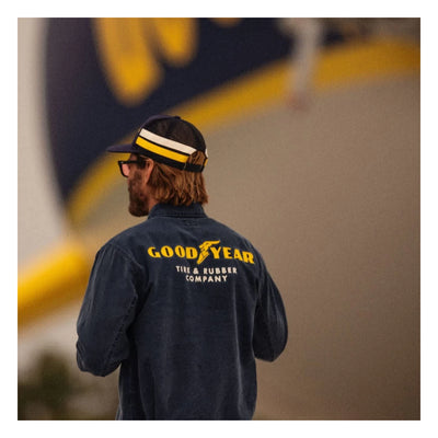 Person wearing Goodyear Trademark LW Washed Navy Jacket, Person wearing jacket near vintage race track with yellow and white