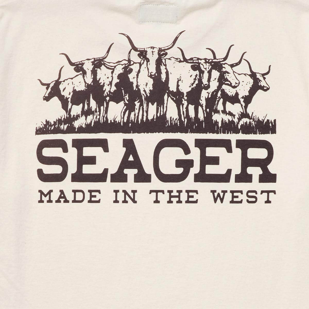 Close-up of Herd Vintage White Tee showing Brown longhorn cattle herd graphic with grass line and bold typeface below -