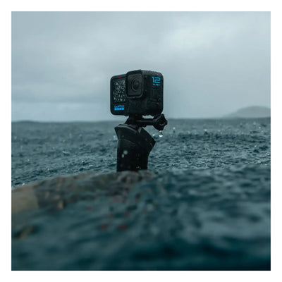 Person wearing Hero 12 Camera Black Camera, Action camera mounted on tripod in shallow ocean water with waves and cloudy sky