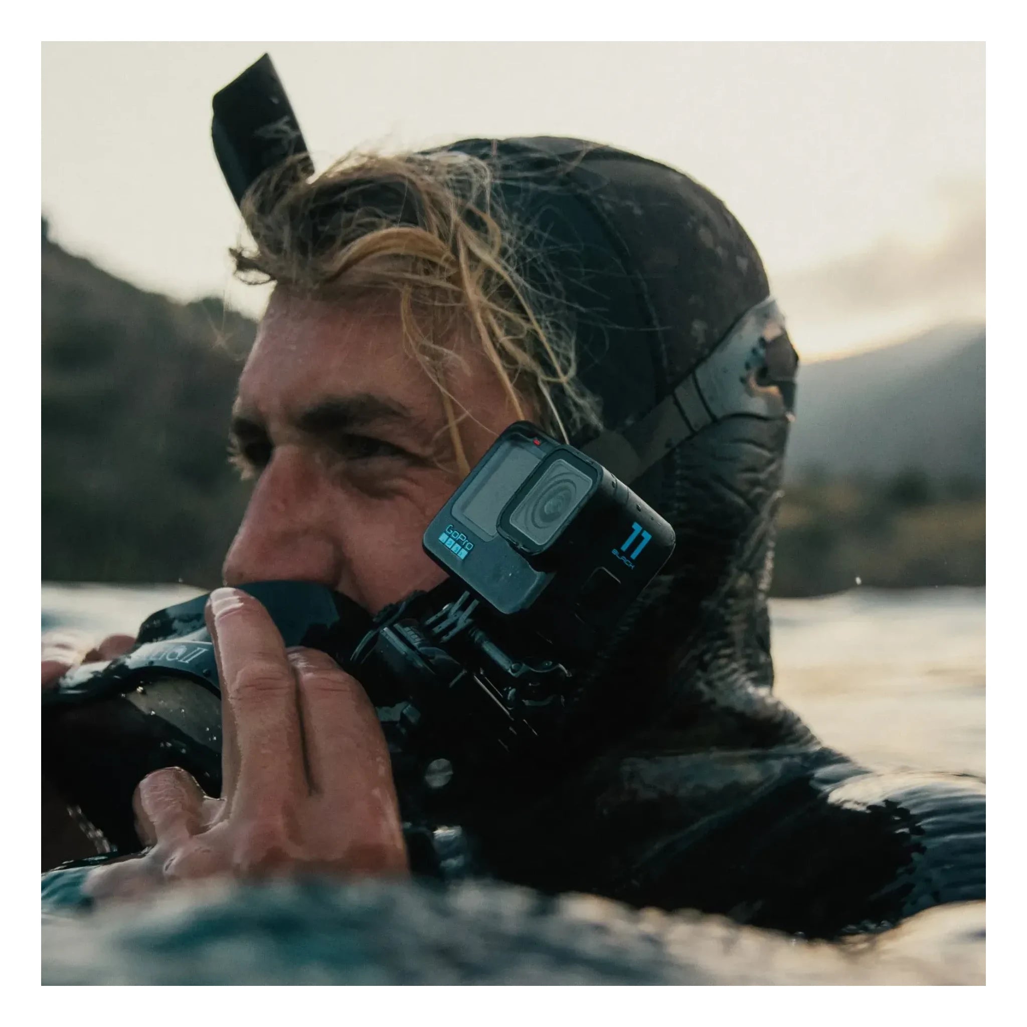 Person wearing Hero 11 Camera Black Camera, Person in water wearing black wetsuit and hood, mountains and lake in background