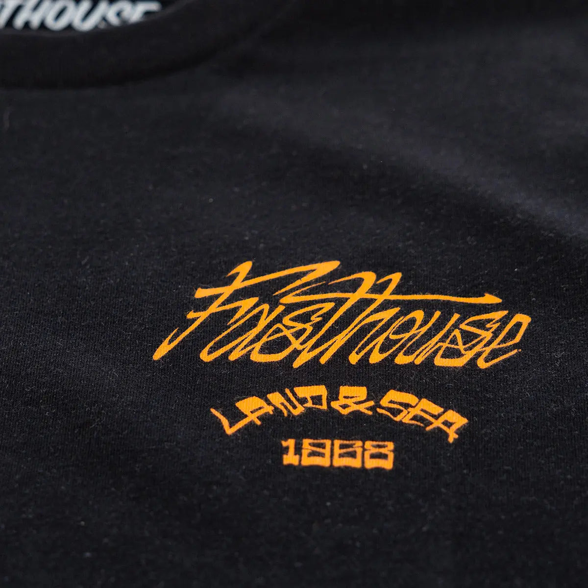 Close-up of Horizon Black Tee showing Gold embroidered script logo with Asian characters and 1983 date on black fabric -