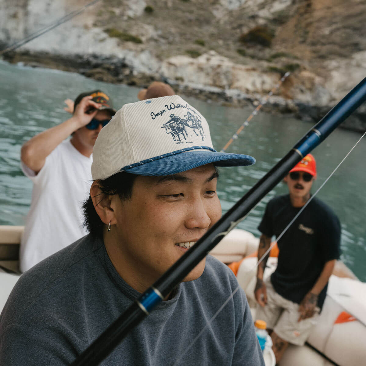 Person wearing Los Rios Cordouroy Snapback Cream/green Hat, Boat on water with rocky cliffs and fishing gear visible -