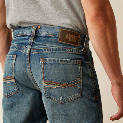 Person wearing M4 M Series Bootcut Scoundrel Pants Pants, Man wearing jeans standing against neutral studio background -