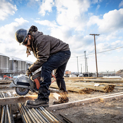 Person wearing M4 Rebar Straight Leg Pants Black Pants, Industrial yard with machinery, steel materials, and power lines