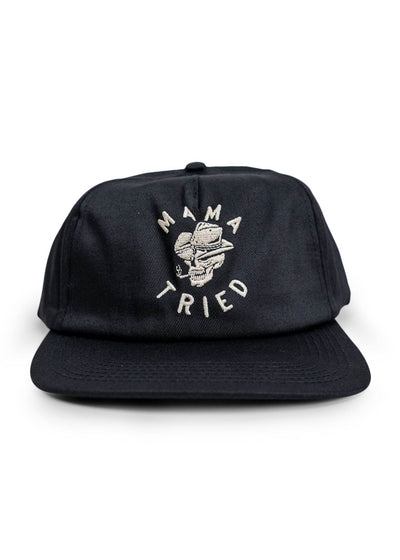Mama Tried front view, Black snapback with cream embroidered skull and crossed wrenches graphic, text arranged in circle