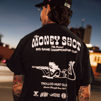 Person wearing Money Shot Heavyweight Tee, Urban street at dusk with industrial buildings and neon lights - Slowride Supply